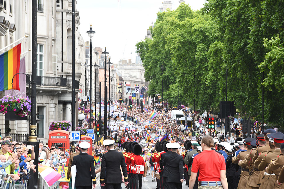 a long shot of streets at pride with people in military uniform in the foreground